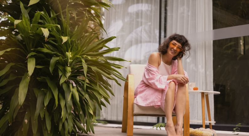 Mulher jovem sorrindo em varanda com plantas, transmitindo bem-estar e estilo de vida saudável em ambiente residencial